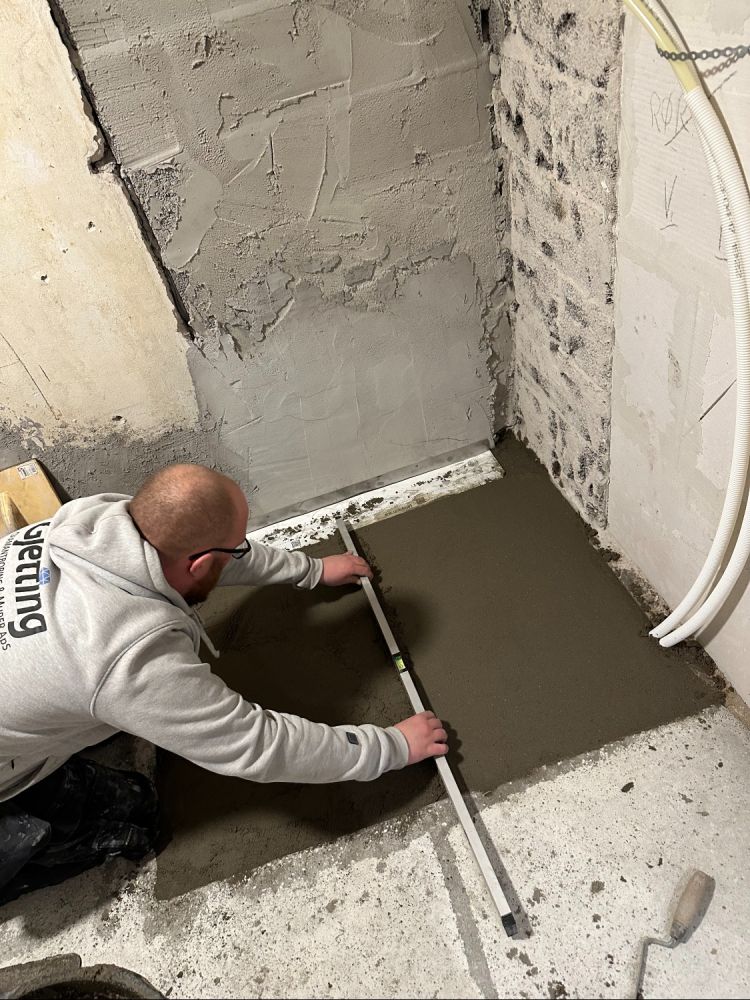 Håndværker nivellerer frisk beton på badeværelsesgulv
